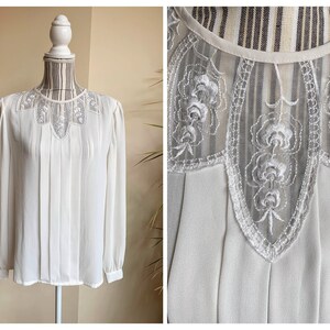 Puede incluir: Blusa blanca de gasa con cuello de encaje y mangas largas. El encaje tiene un delicado patr&oacute;n floral.