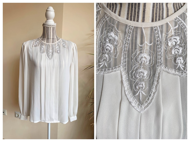 Puede incluir: Blusa blanca de gasa con cuello de encaje y mangas largas. El encaje tiene un delicado patr&oacute;n floral.