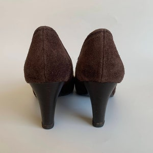 May include: A pair of brown suede heeled shoes with a pointed toe. The shoes are shown from the back.