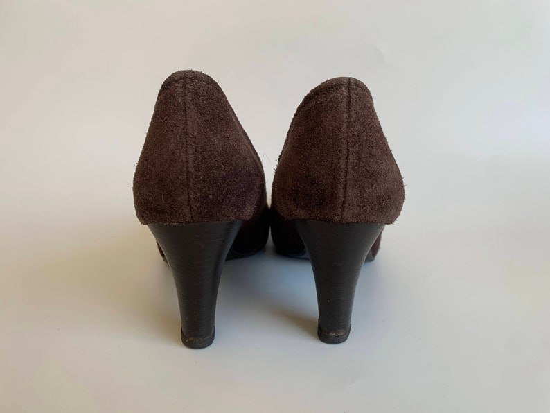 May include: A pair of brown suede heeled shoes with a pointed toe. The shoes are shown from the back.