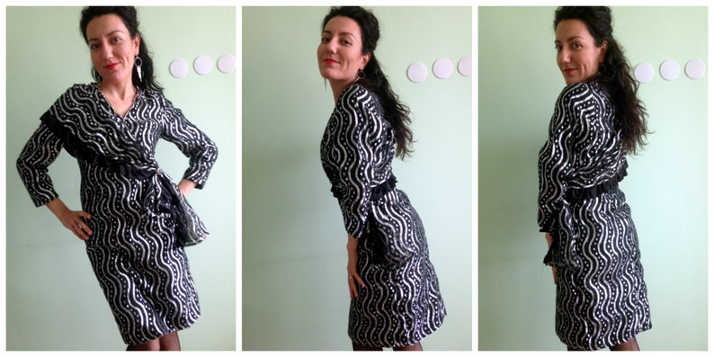 May include: A black and silver dress with a wavy pattern. The dress has long sleeves and a V-neckline. It is cinched at the waist with a black belt.