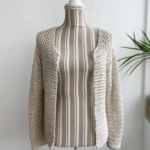 May include: A cream-colored crochet cardigan with a loose fit and long sleeves. The cardigan is made of a lightweight, open-weave fabric.