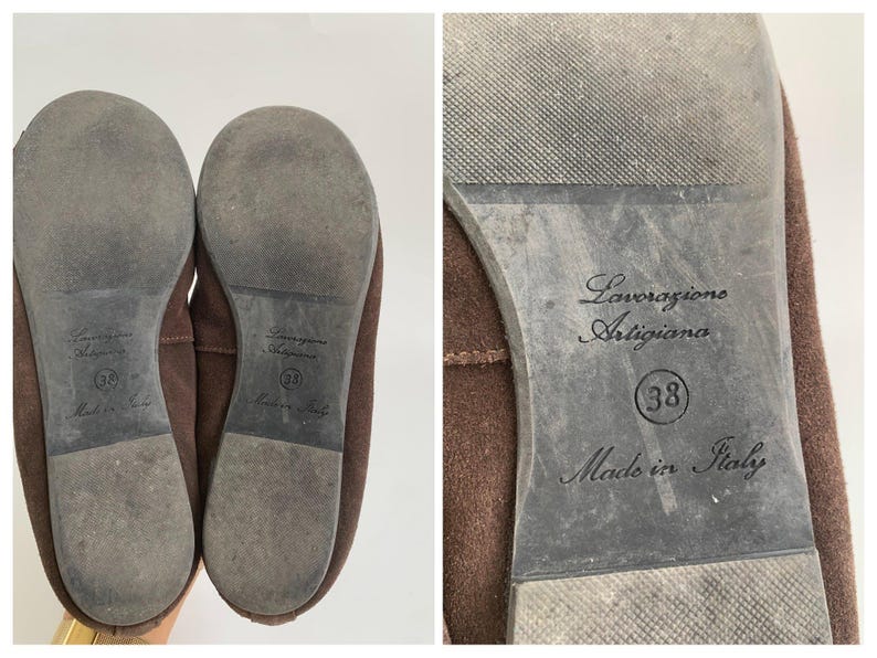 May include: Pair of brown suede flats. The soles are gray with the text "Lavorazione Artigiana", size 38, and "Made in Italy". The shoes are a neutral color and appear to be unworn.