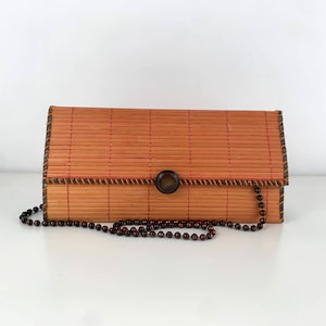May include: A brown woven bamboo clutch bag with a brown button closure and a brown beaded chain strap.