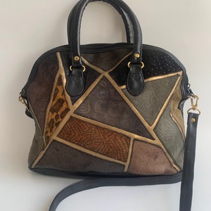 Peut inclure: Un sac à main en cuir noir avec un design patchwork présentant différentes nuances de brun, beige et vert. Le sac a deux poignées supérieures et une longue bandoulière réglable.