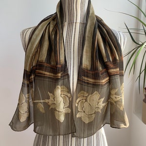 May include: A brown and beige silk scarf with a floral pattern and abstract design. The scarf is draped over a mannequin.