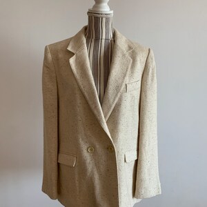 Peut inclure: Un blazer beige &agrave; double boutonnage avec un motif mouchet&eacute;. Le blazer a deux poches sur le devant et un seul bouton sur chaque poignet.
