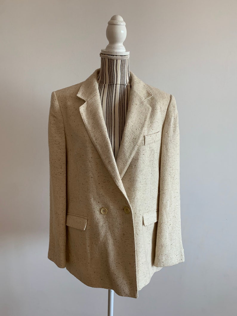 Peut inclure: Un blazer beige &agrave; double boutonnage avec un motif mouchet&eacute;. Le blazer a deux poches sur le devant et un seul bouton sur chaque poignet.