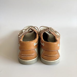 May include: A pair of brown and white leather boat shoes with laces. The shoes have a brown leather upper and a white rubber sole.