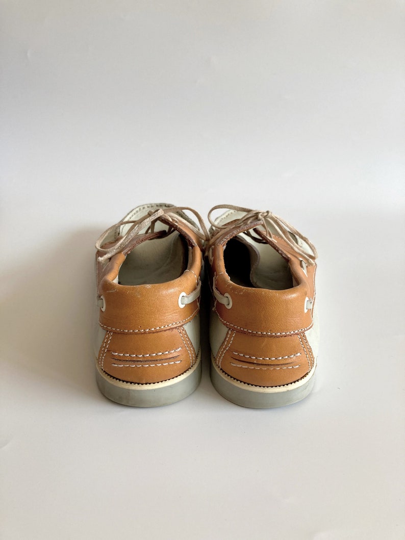 May include: A pair of brown and white leather boat shoes with laces. The shoes have a brown leather upper and a white rubber sole.