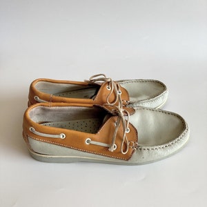 May include: A pair of light gray leather boat shoes with brown leather trim and laces.