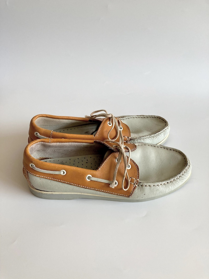 May include: A pair of light gray leather boat shoes with brown leather trim and laces.