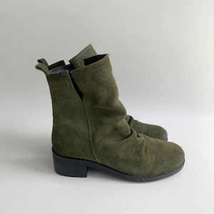 May include: Green suede ankle boots with a low block heel. The boots have a slouchy, relaxed fit.