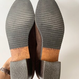 May include: A pair of brown suede ankle boots with a block heel. The boots are size 39 and say "Made in Italy" on the soles.