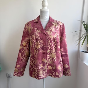 Può includere: Un blazer a maniche lunghe nei toni del magenta e del beige, caratterizzato da un evidente motivo leopardato sovrapposto a disegni floreali stilizzati. Il capo presenta un colletto a revers, chiusura frontale con bottoni e una trama a spina di pesce.
