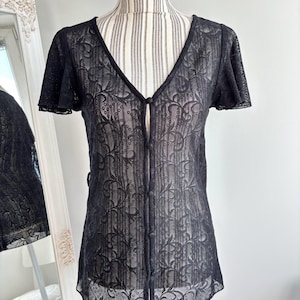 Puede incluir: Una blusa negra transparente con botones, estampado floral y mangas cortas.