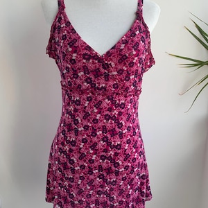 May include: A sleeveless, floral-print top in shades of pink and dark purple, displayed on a mannequin. The top features a V-neckline and delicate spaghetti straps. The fabric is covered in a small, repeating floral pattern.