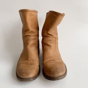 May include: A pair of brown leather ankle boots with a slouchy look. The boots have a rounded toe and a low heel.