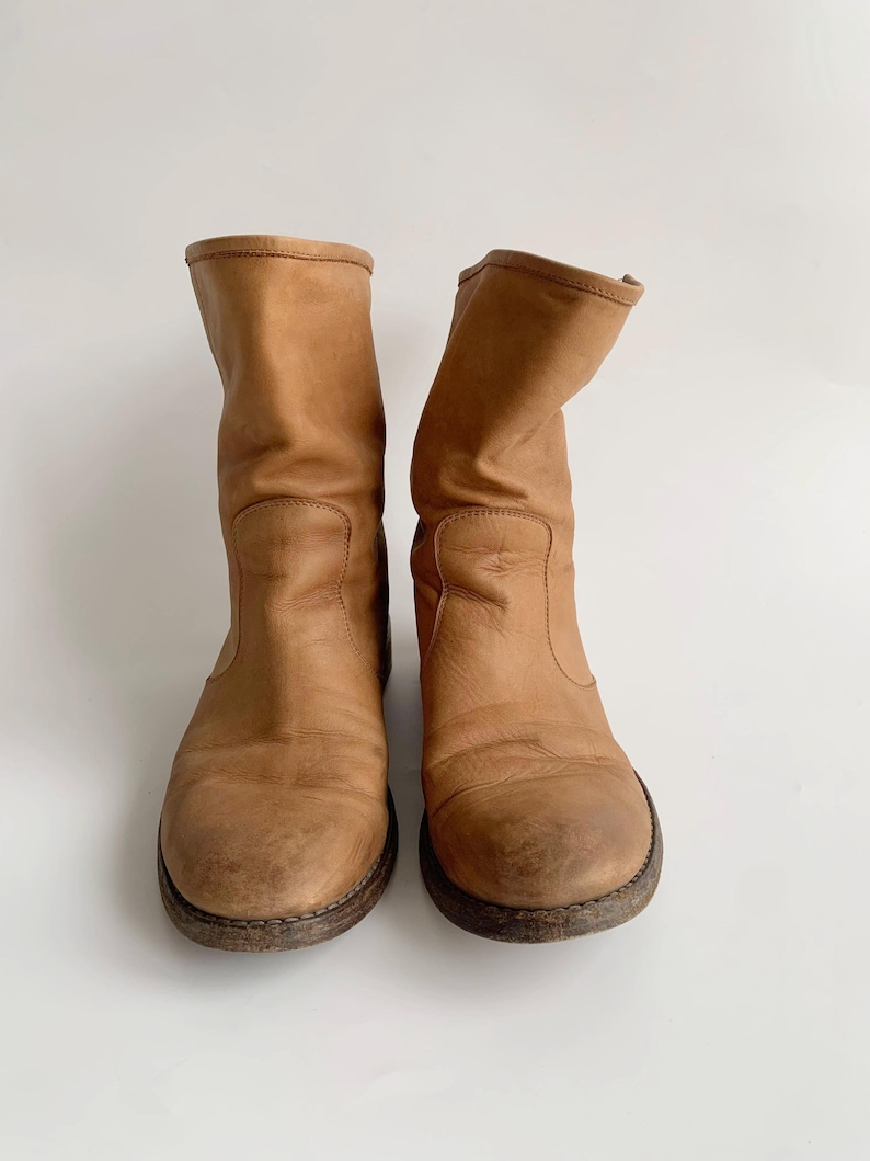 May include: A pair of brown leather ankle boots with a slouchy look. The boots have a rounded toe and a low heel.