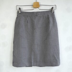 May include: A black and white houndstooth pattern skirt hanging on a wooden hanger. The skirt is a classic style, with a straight cut and a tailored waistband. The fabric has a small, repeating check pattern.