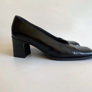 May include: A pair of black leather pumps with a square toe and a block heel. The heels are approximately 3 inches high. The shoes have a classic, minimalist design.