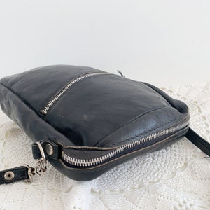 Pu&ograve; includere: Una borsa a tracolla in pelle nera con chiusura a zip e una tracolla a catena argentata.