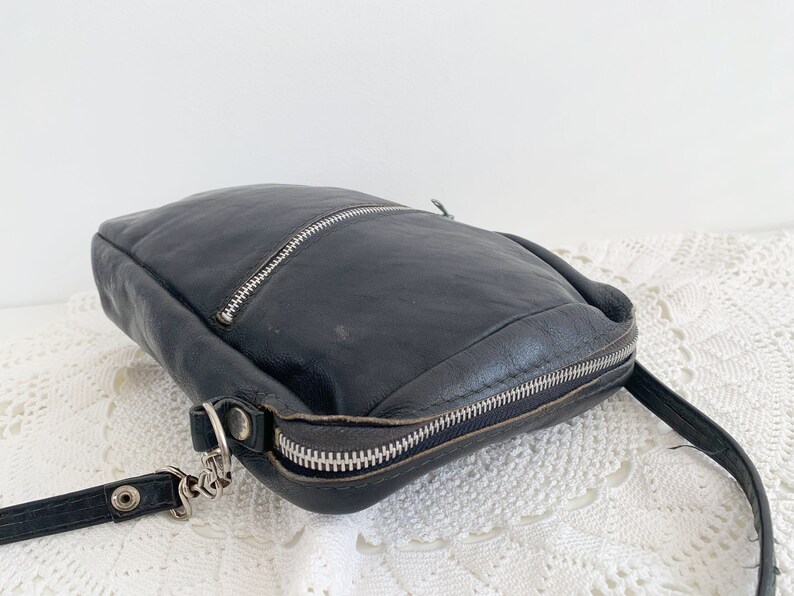 Pu&ograve; includere: Una borsa a tracolla in pelle nera con chiusura a zip e una tracolla a catena argentata.