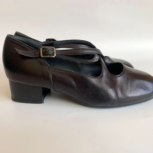 Pu&ograve; includere: Scarpe con tacco in pelle nera con fibbia e cinturini incrociati.