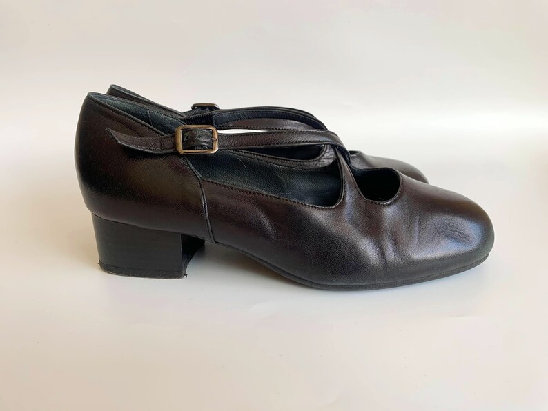 Pu&ograve; includere: Scarpe con tacco in pelle nera con fibbia e cinturini incrociati.