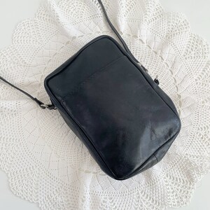 Pu&ograve; includere: Una borsa a tracolla in pelle nera con un design semplice. La borsa ha una chiusura a lembo e un unico cinturino.