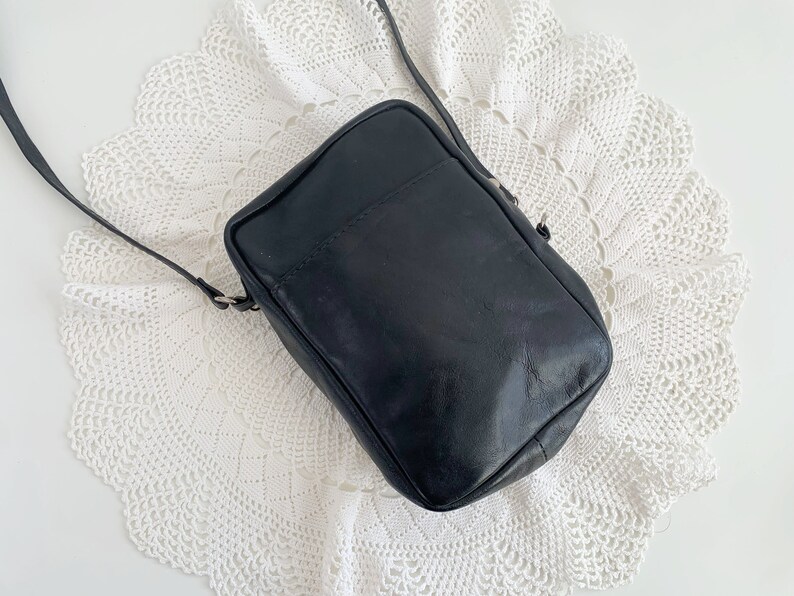 Pu&ograve; includere: Una borsa a tracolla in pelle nera con un design semplice. La borsa ha una chiusura a lembo e un unico cinturino.