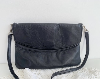 Könnte beinhalten: Eine schwarze Lederschultertasche mit Klappenverschluss und einer silbernen Schnalle. Die Tasche hat eine strukturierte Oberfläche und einen langen Riemen.