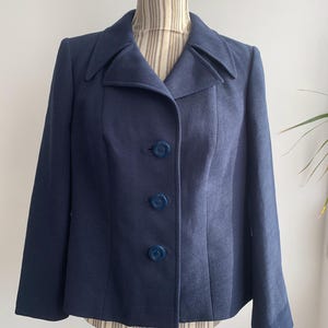 Könnte beinhalten: Ein marineblauer Blazer mit Reverskragen und vier blauen Knöpfen. Der Blazer ist tailliert und hat eine figurbetonte Silhouette.