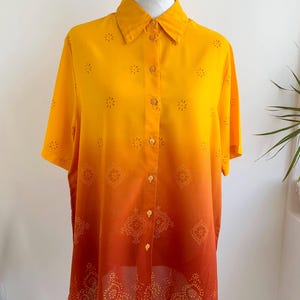 Può includere: Camicia button-down a maniche corte con un design sfumato dal giallo all'arancione. La camicia presenta motivi decorativi traforati e un design a pois dettagliato sull'orlo. Esposta su un manichino.