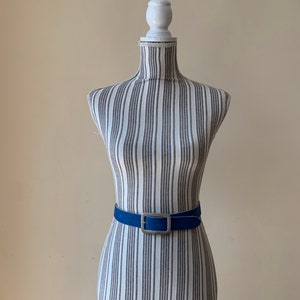Pu&ograve; includere: Una cintura in pelle blu con una fibbia argentata su un manichino bianco.