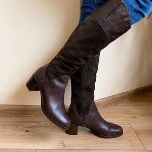 May include: Brown leather knee-high boots with a suede panel and a block heel.