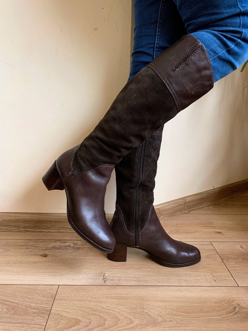 May include: Brown leather knee-high boots with a suede panel and a block heel.
