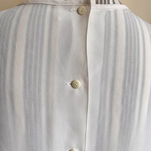 Puede incluir: Camisa blanca de botones con estampado de rayas. La camisa tiene tres botones en la espalda.