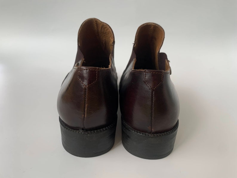 K&ouml;nnte beinhalten: Ein Paar braune Lederstiefeletten mit spitzer Zehenpartie und niedrigem Absatz. Die Stiefeletten haben einen Pull-on-Stil und ein glattes Lederfinish.