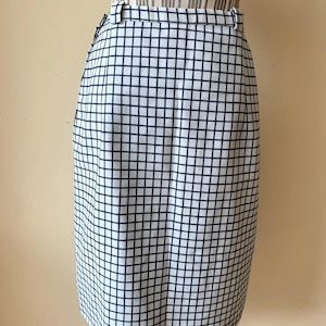 Può includere: Una gonna bianca con un motivo a quadri bianco e nero. La gonna ha una cintura e una silhouette dritta.