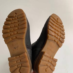 May include: A pair of black ankle boots with dark leather uppers and thick, gum-coloured rubber lug soles. The outsoles feature a deep tread pattern for traction, with the number 39 embossed on the arch area of each sole and a side zip fastening.