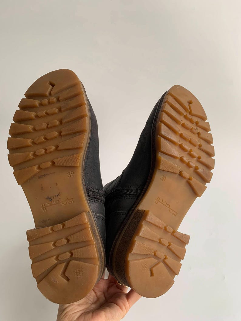 May include: A pair of black ankle boots with dark leather uppers and thick, gum-coloured rubber lug soles. The outsoles feature a deep tread pattern for traction, with the number 39 embossed on the arch area of each sole and a side zip fastening.