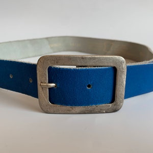 Pu&ograve; includere: Una cintura in pelle blu con una fibbia argentata. La cintura &egrave; realizzata in pelle morbida e flessibile e ha un design classico.