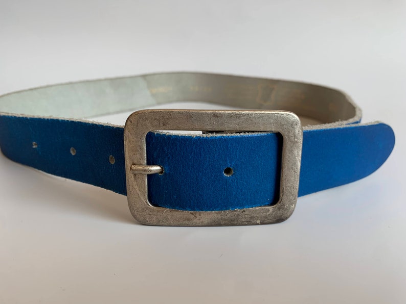 Pu&ograve; includere: Una cintura in pelle blu con una fibbia argentata. La cintura &egrave; realizzata in pelle morbida e flessibile e ha un design classico.