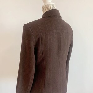 May include: A brown blazer with thin white pinstripes. The blazer has a single button closure and long sleeves.