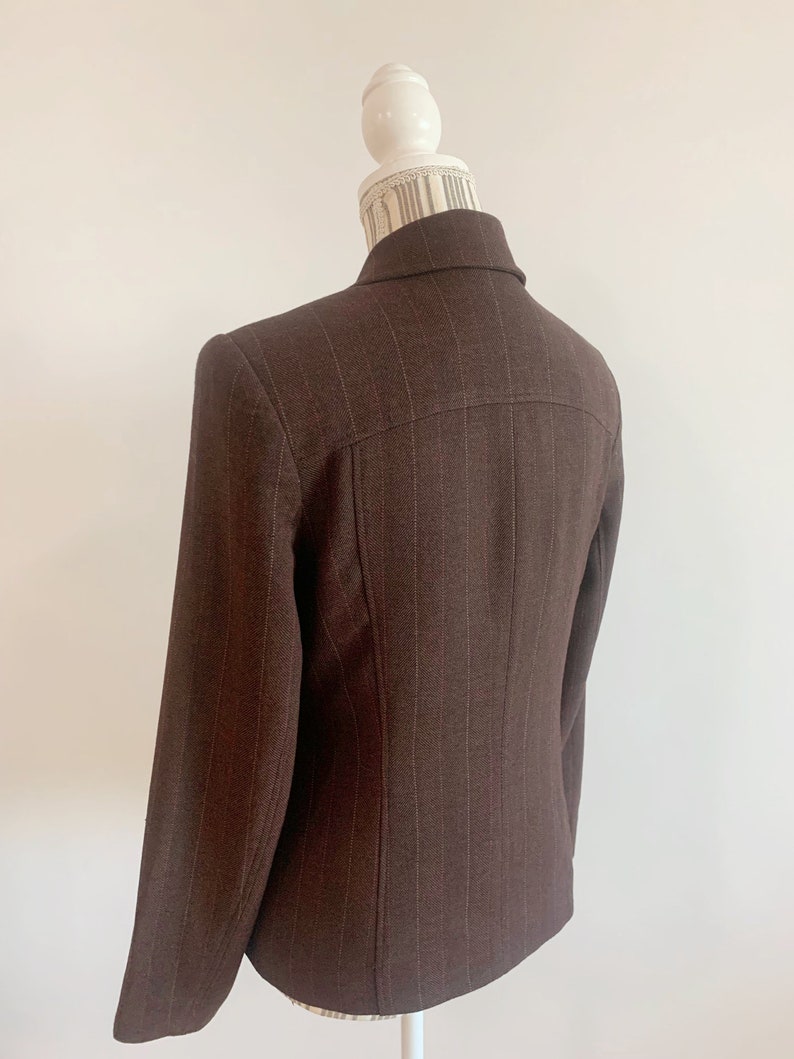May include: A brown blazer with thin white pinstripes. The blazer has a single button closure and long sleeves.