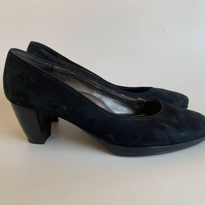 May include: A pair of black suede heeled pumps with a block heel.