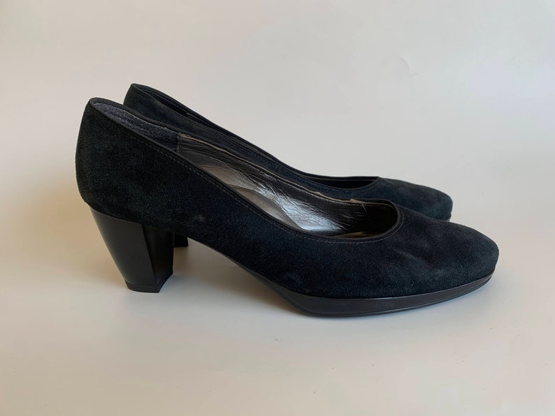 May include: A pair of black suede heeled pumps with a block heel.