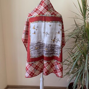 May include: A red and white plaid scarf with a white center panel featuring a scene of ducks flying over a lake. The center panel is bordered by a red and gold patterned frame.