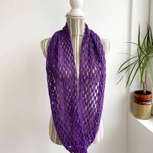 May include: A purple crocheted infinity scarf with a delicate openwork pattern. The scarf is displayed on a white mannequin.